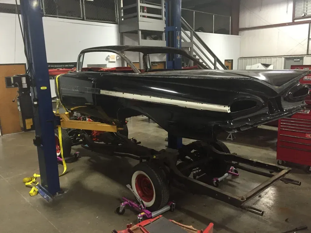 Black classic car body on a frame in a garage, undergoing restoration.