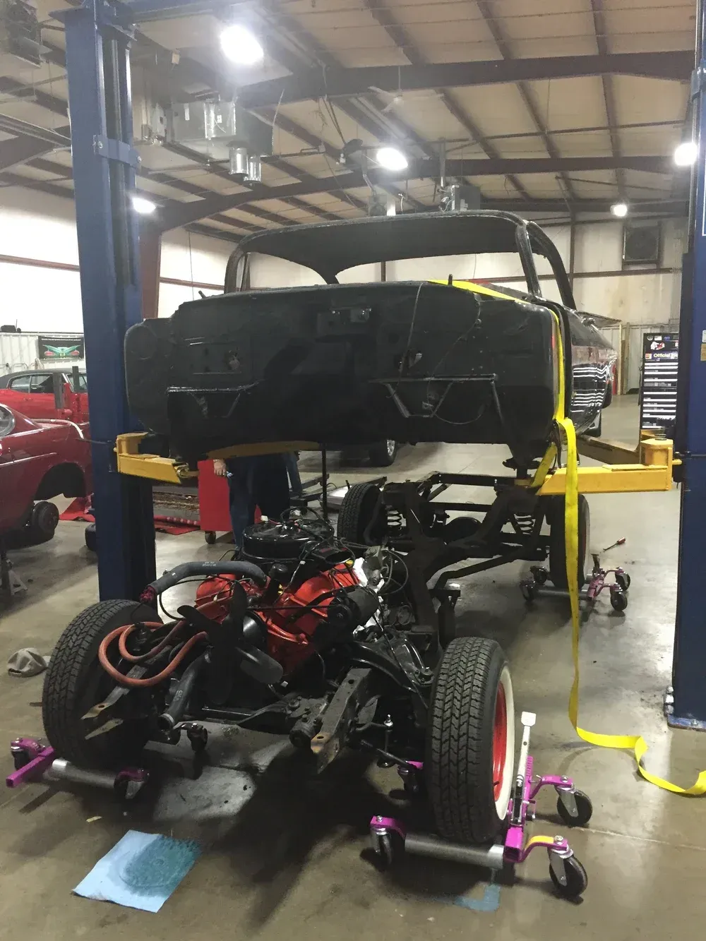 Car chassis and body separated on a lift in a garage.