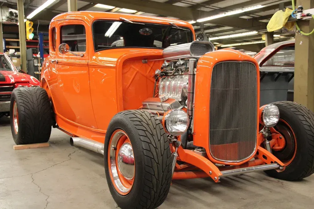 Bright orange classic hot rod with a large engine in a garage.