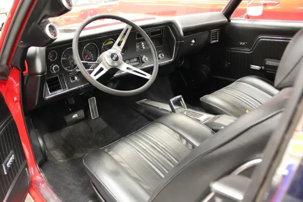 Black interior of a classic red car. Black leather seats, silver steering wheel, and black dashboard.