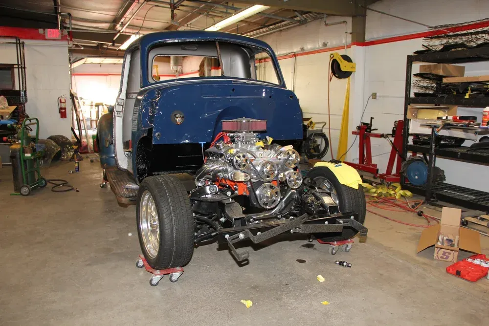 Blue classic truck being restored in a garage. Chassis on dollies, engine installed, body partially assembled.