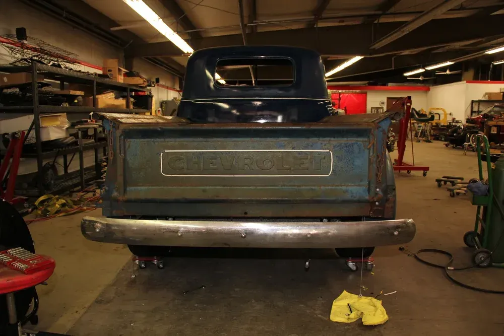 Back view of a vintage blue Chevrolet pickup truck in a garage.