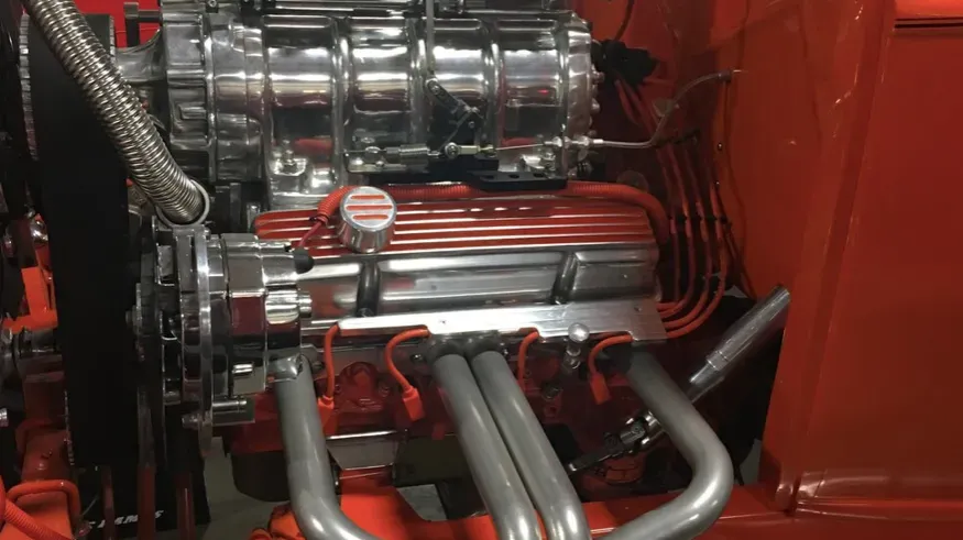 Close-up of a shiny, modified car engine. Chrome and red components visible, with exhaust headers.