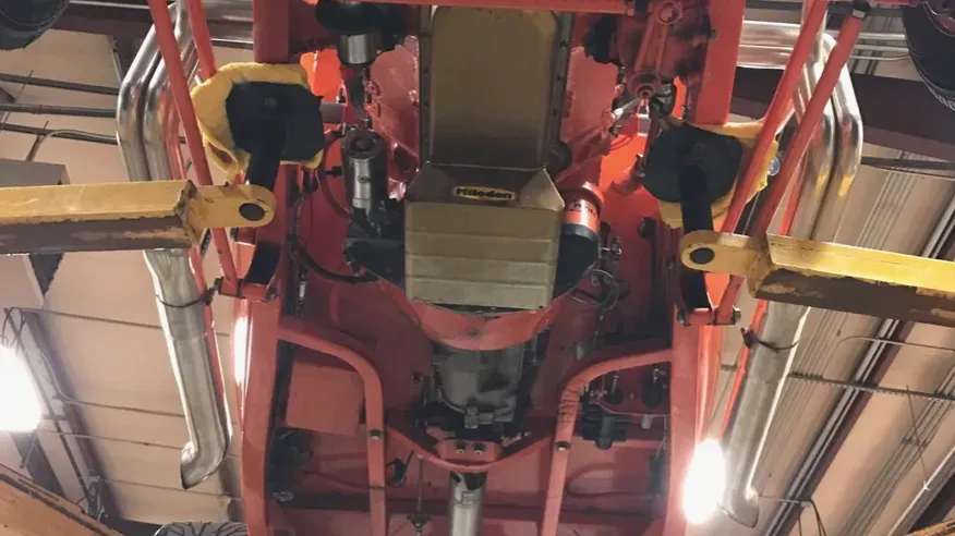 Underside of a bright red car on a lift in a garage, showing engine and exhaust system.