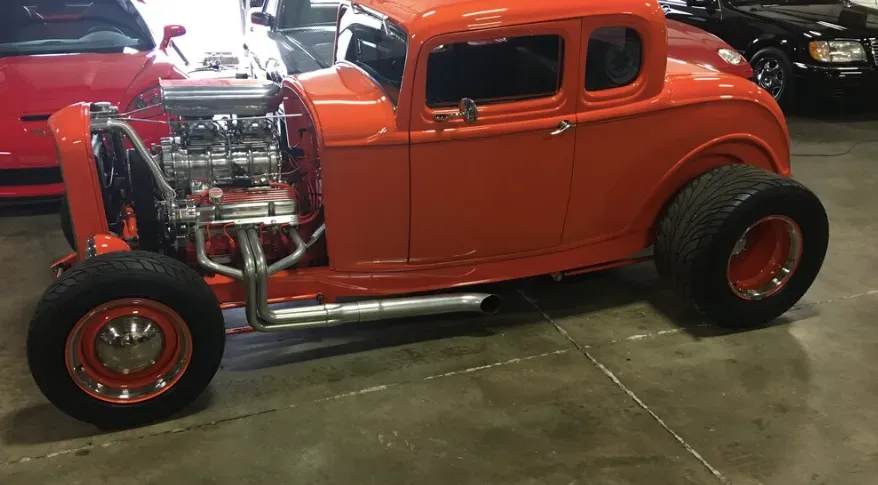 Orange hot rod with exposed engine and chrome accents on a concrete floor.