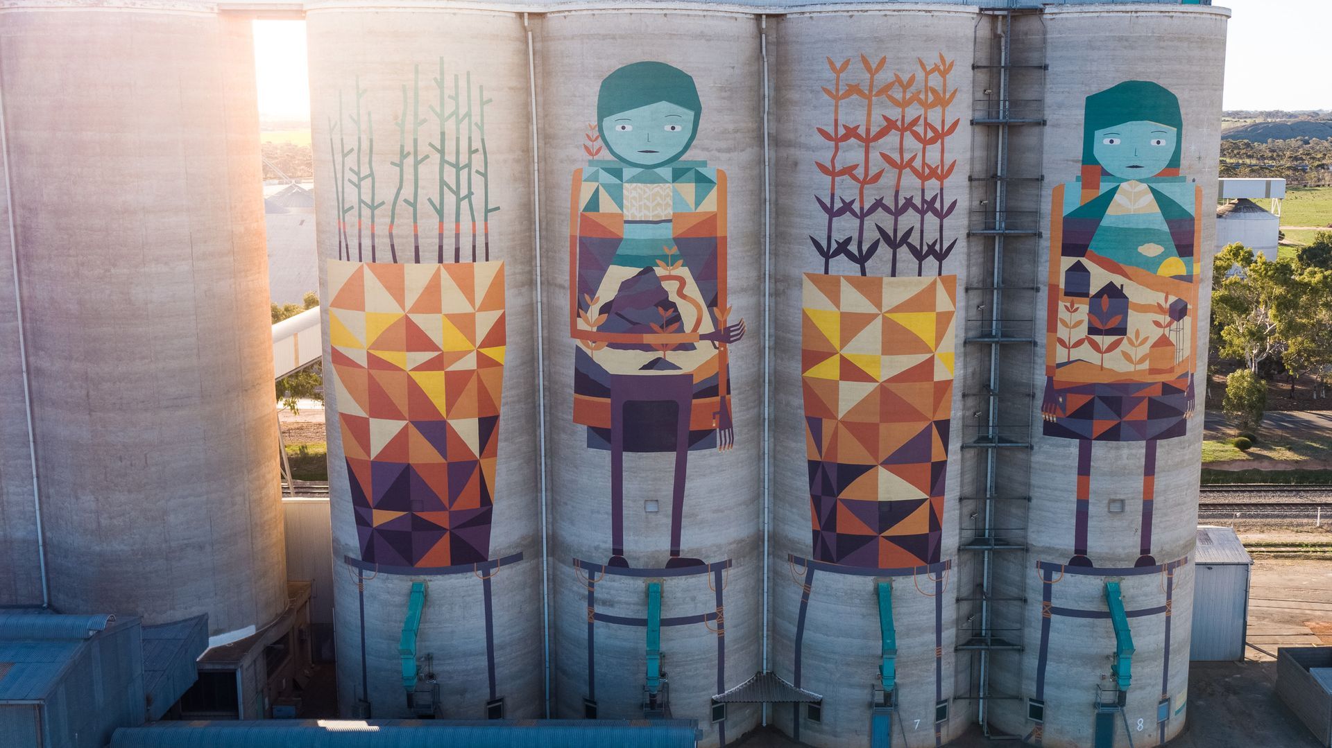 Colorful silo murals depicting figures and geometric patterns; outdoor setting. 