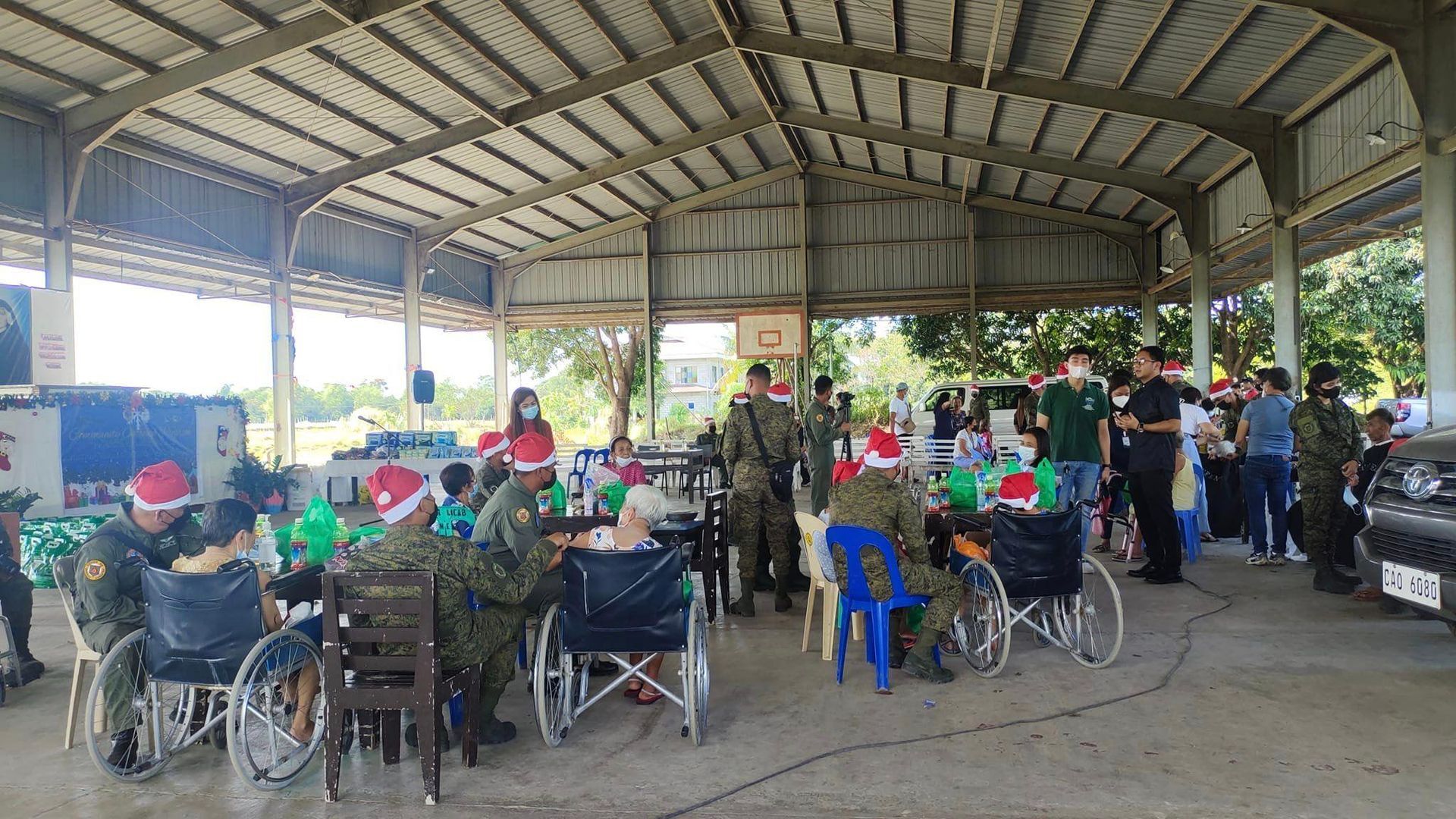 A group of people in wheelchairs are sitting at tables under a covered area.