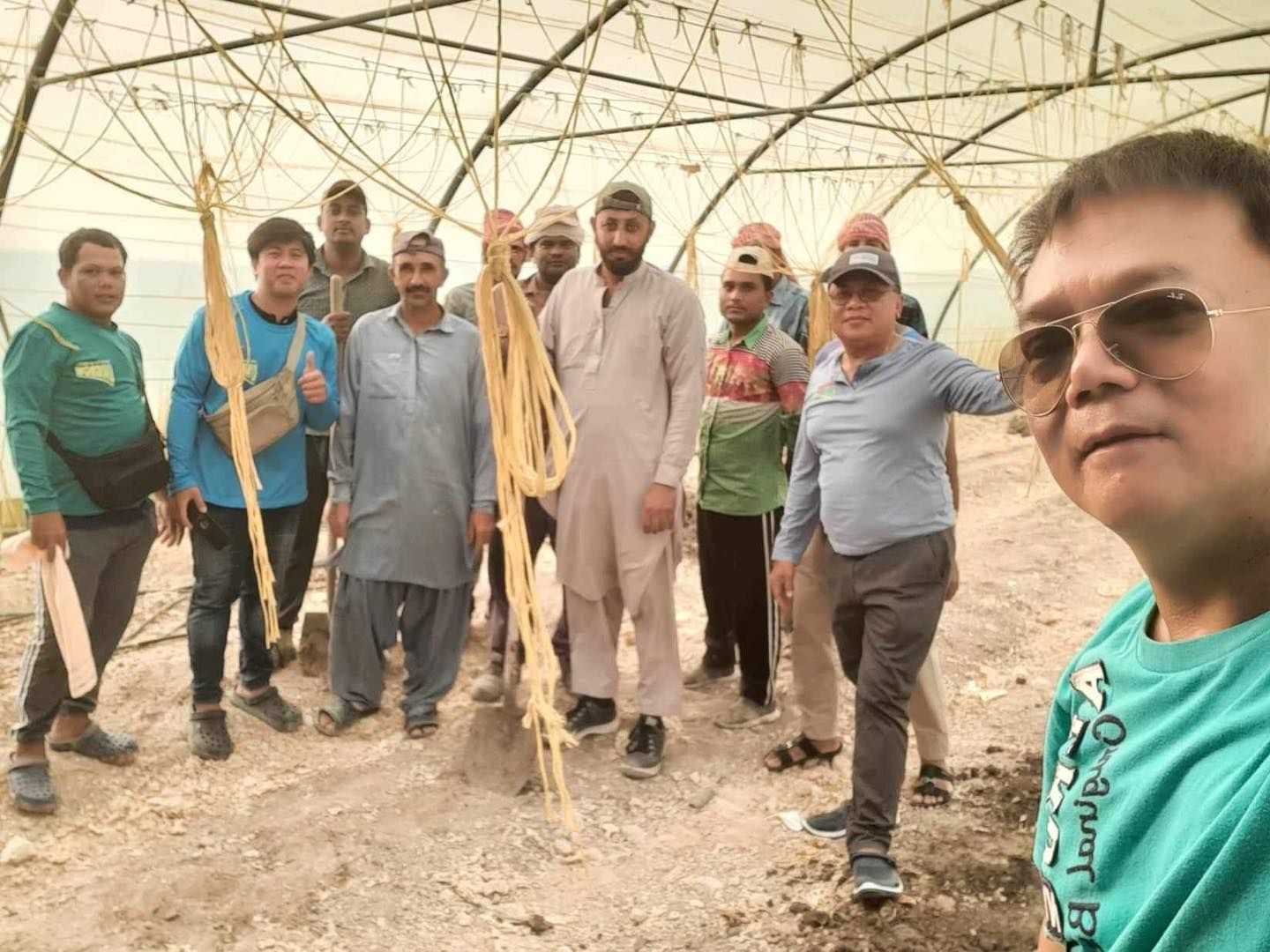 A group of men are standing in front of a greenhouse.