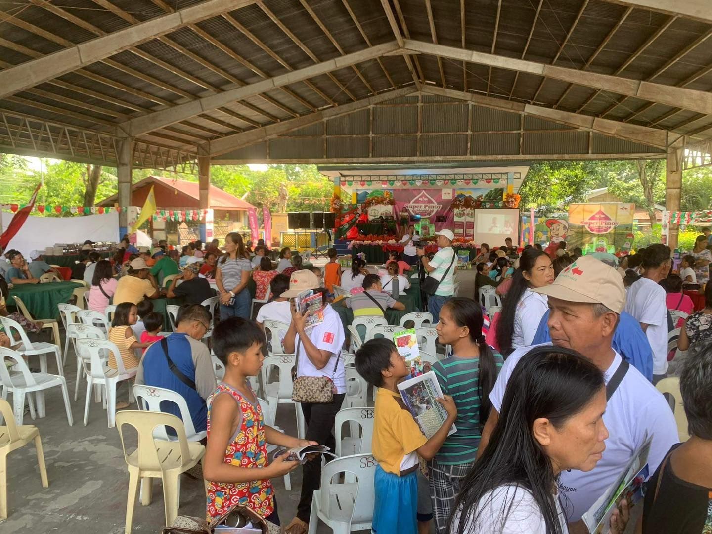 A large group of people are sitting in chairs under a covered area.