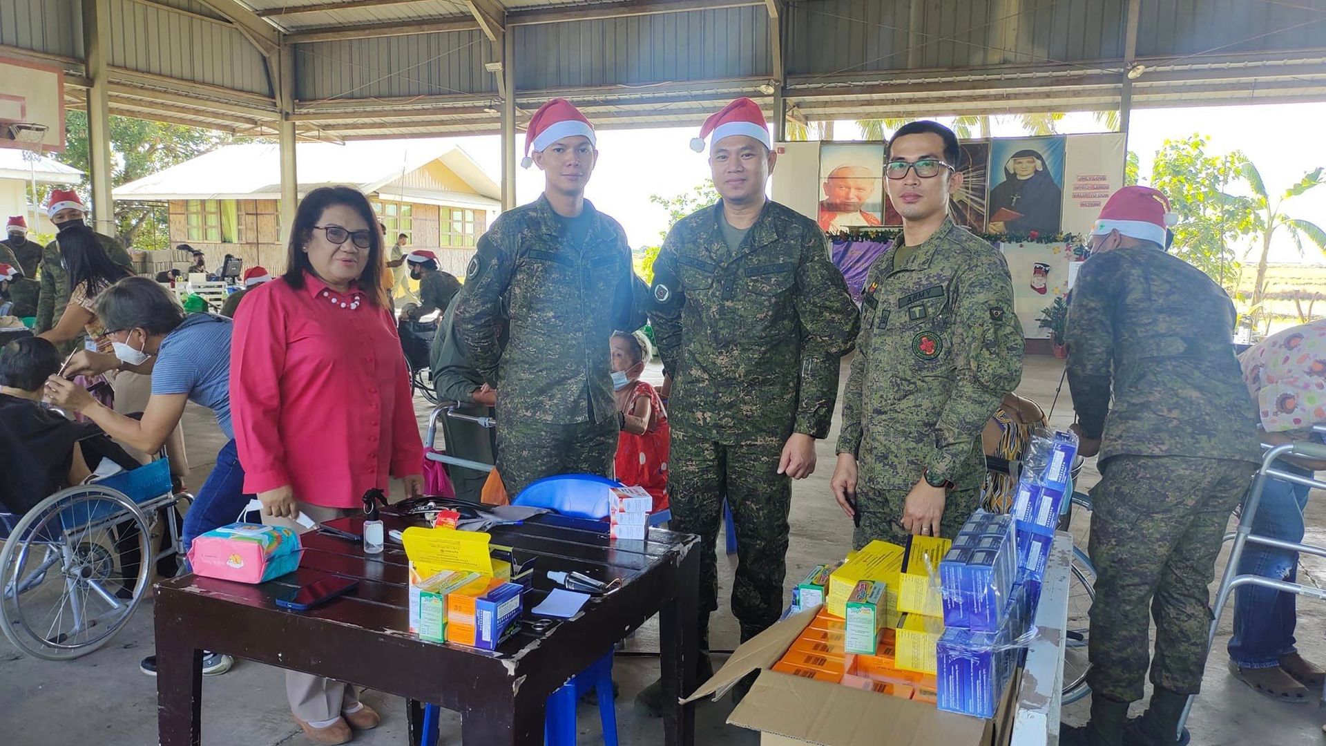 A group of soldiers wearing santa hats are standing around a table.