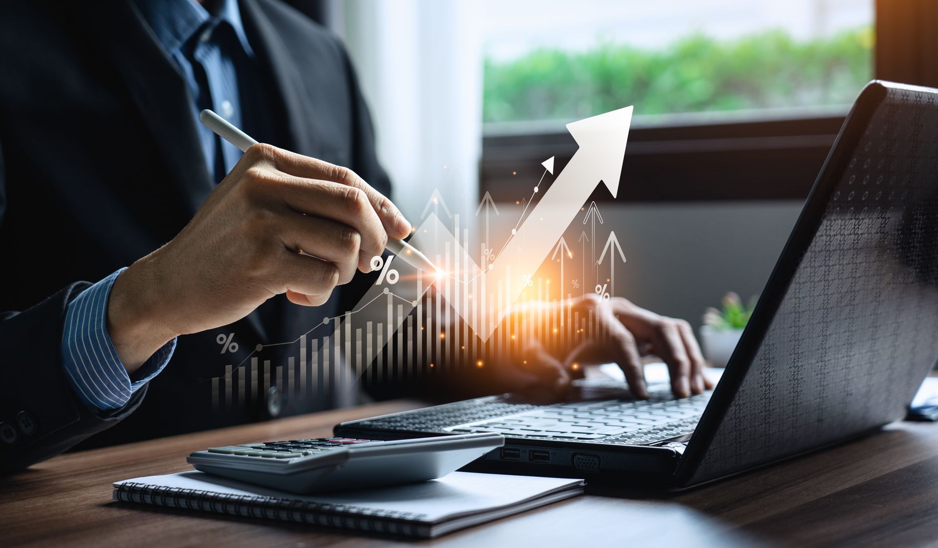 Person in a suit typing on a laptop beside a rising arrow and glowing business chart on a desk