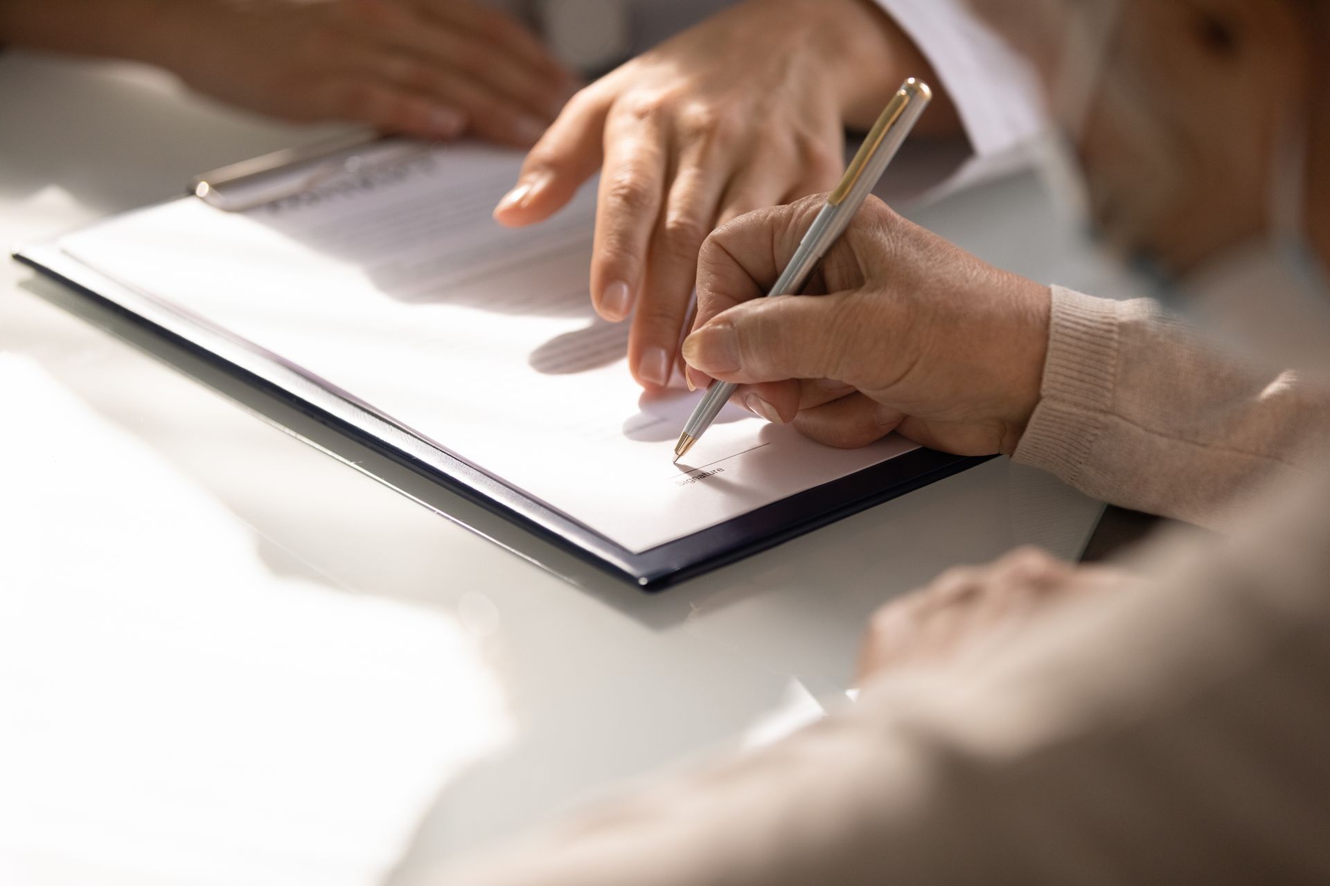 Hands writing in a notebook with a pencil at a table.
