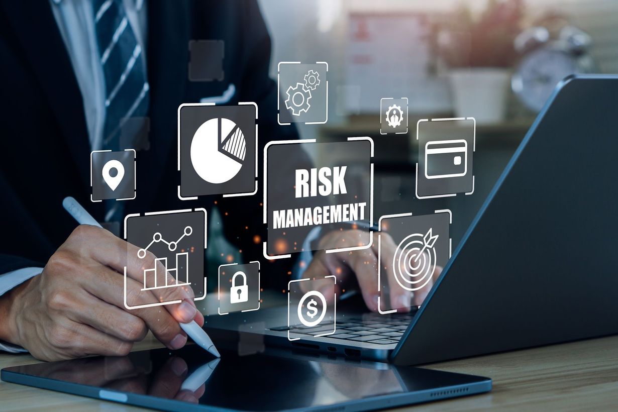 Businessperson using laptop and tablet with risk management icons overlay on a desk