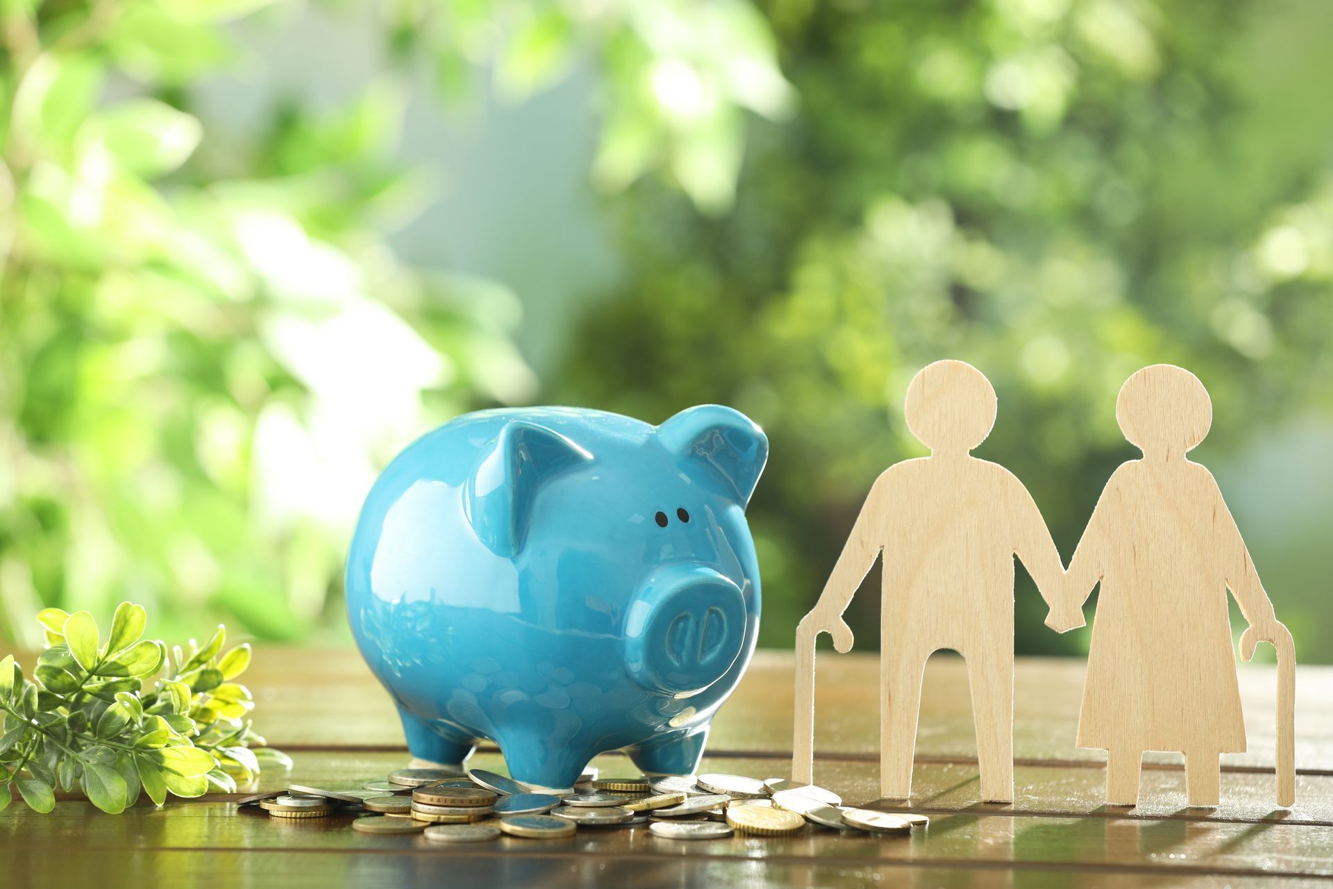 Blue piggy bank beside wooden figures holding hands on stacked coins, with a green blurred background