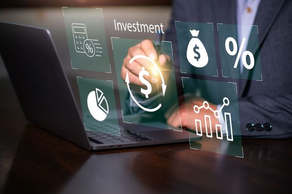 Laptop with holographic investment icons, dollar sign, and rising chart on a dark desk