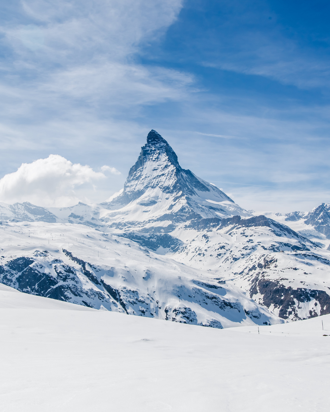 Le Cervin enneigé se détachant sur un ciel bleu parsemé de nuages ​​épars.