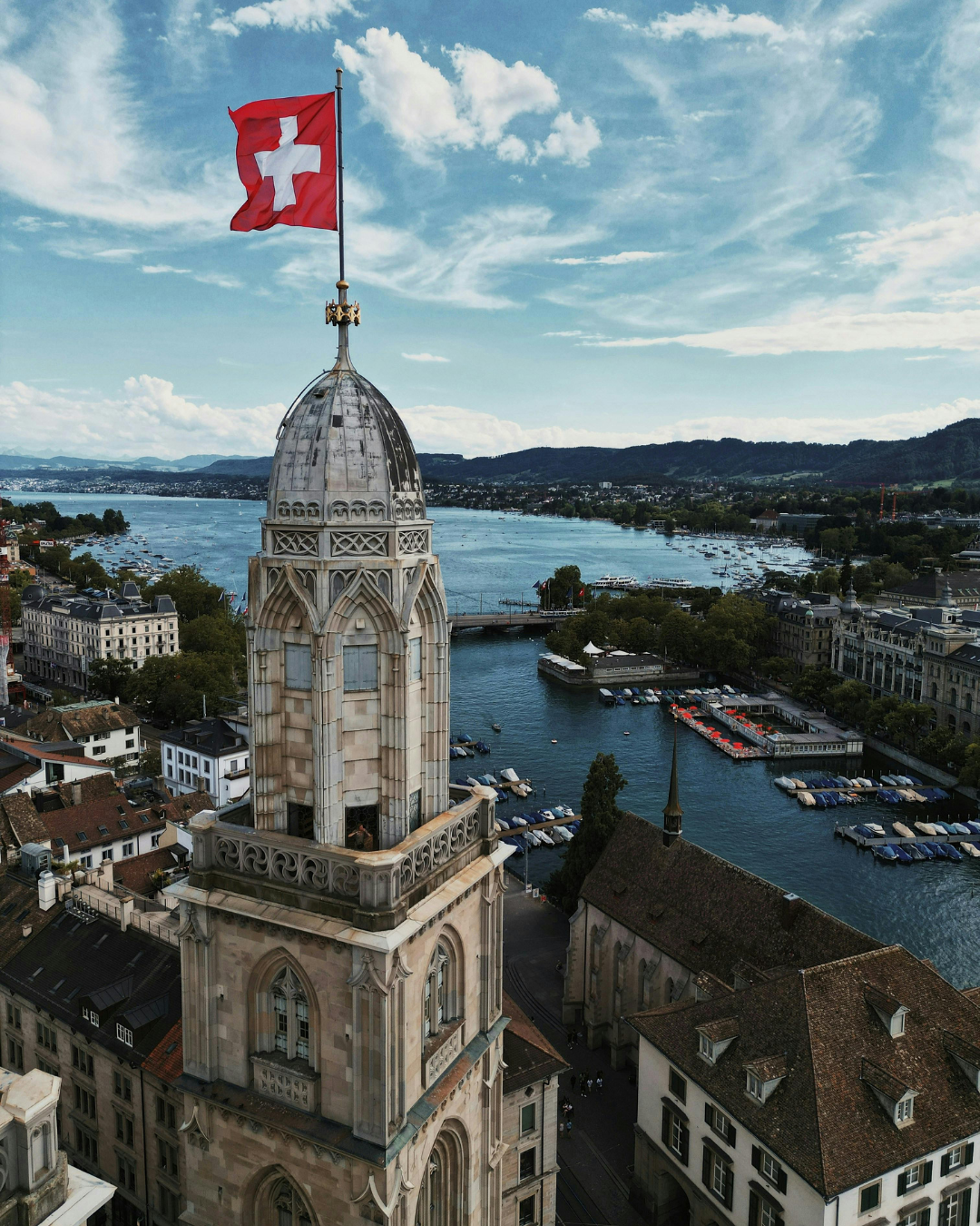 Drapeau suisse flottant au sommet du clocher d'une église surplombant une ville et un lac.