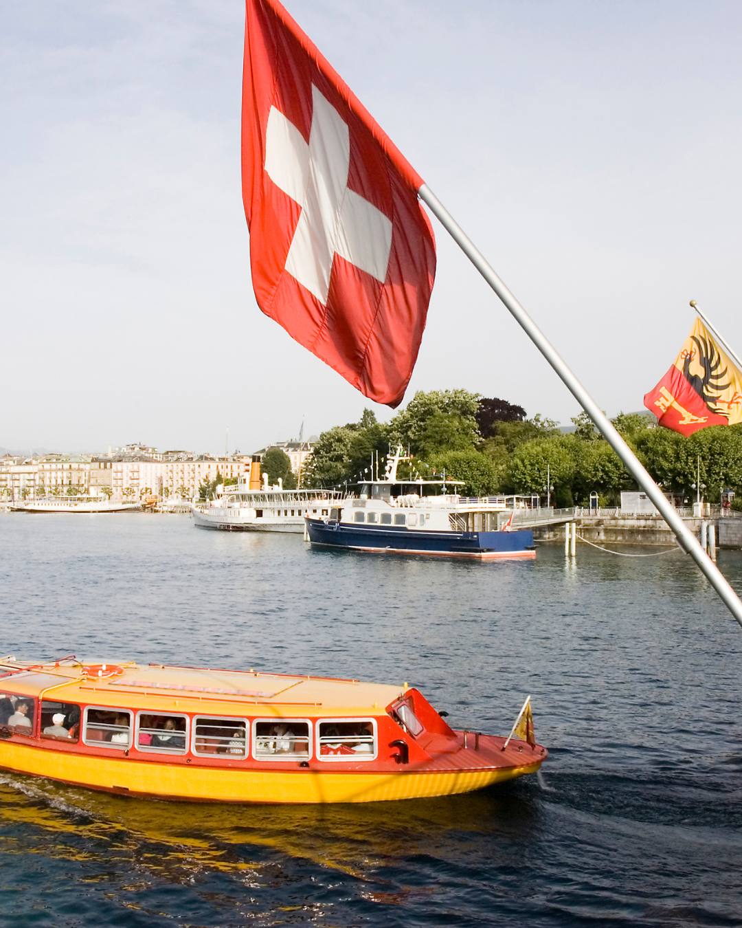 Drapeau suisse flottant au-dessus d'un lac avec des bateaux et une silhouette urbaine.
