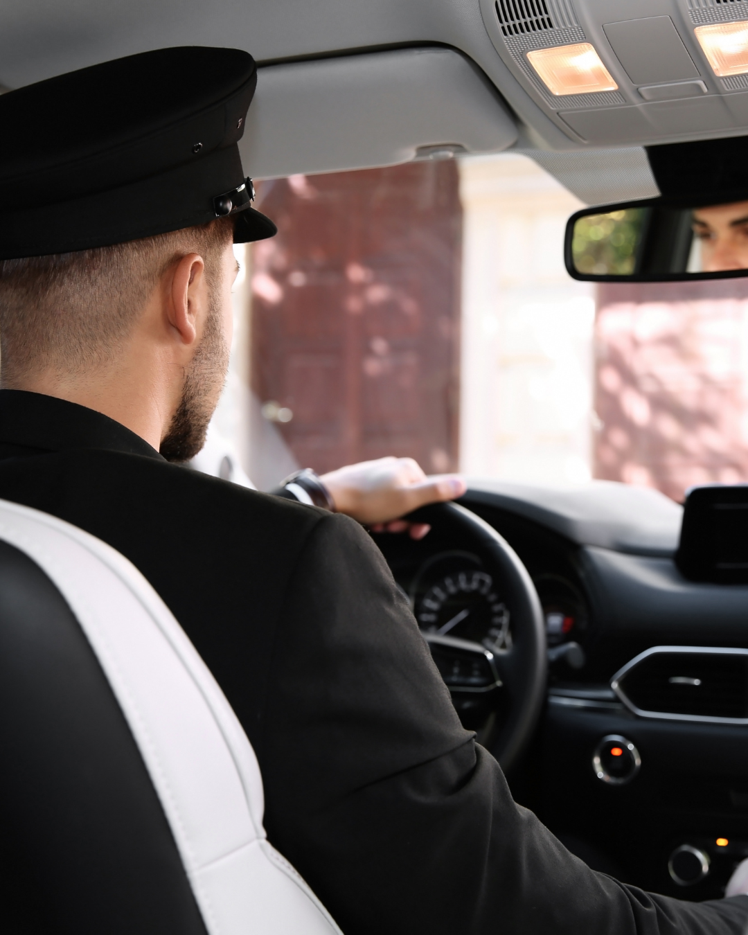 Le chauffeur, en uniforme et casquette noirs, tient le volant. À l'intérieur de la voiture, avec le rétroviseur.