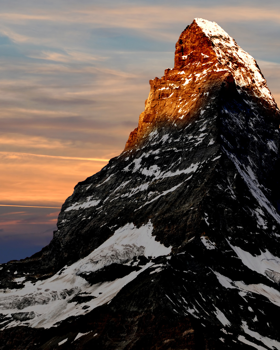 Le sommet enneigé du Cervin, illuminé par la chaude lumière du lever du soleil, se détache sur un ciel aux teintes pastel.