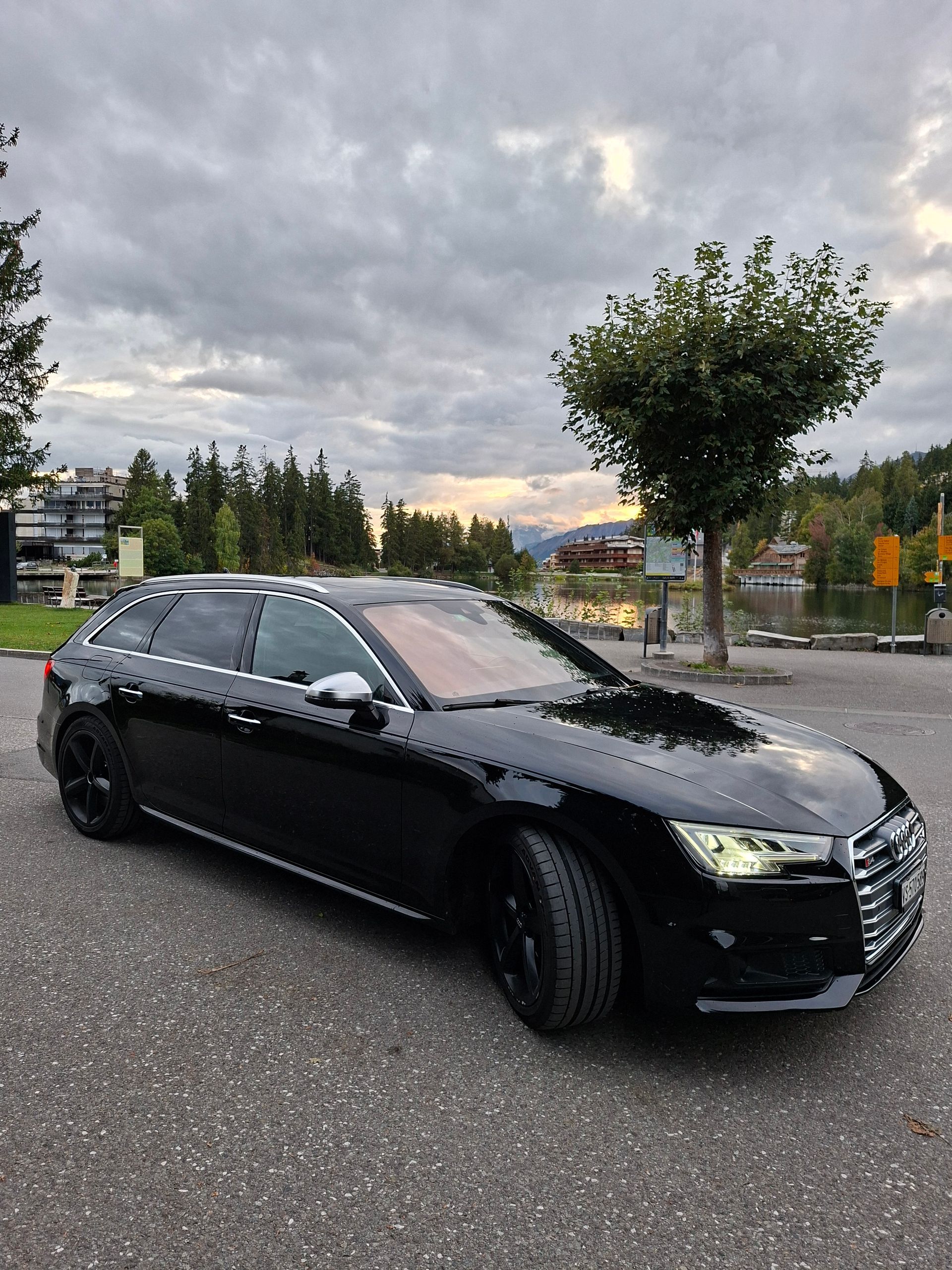 Une Audi break noire garée sur le trottoir sous un ciel nuageux.