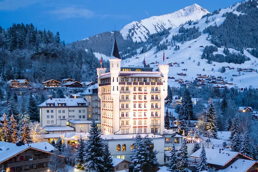 Hôtel suisse enneigé avec tour, entouré d'arbres et de montagnes.