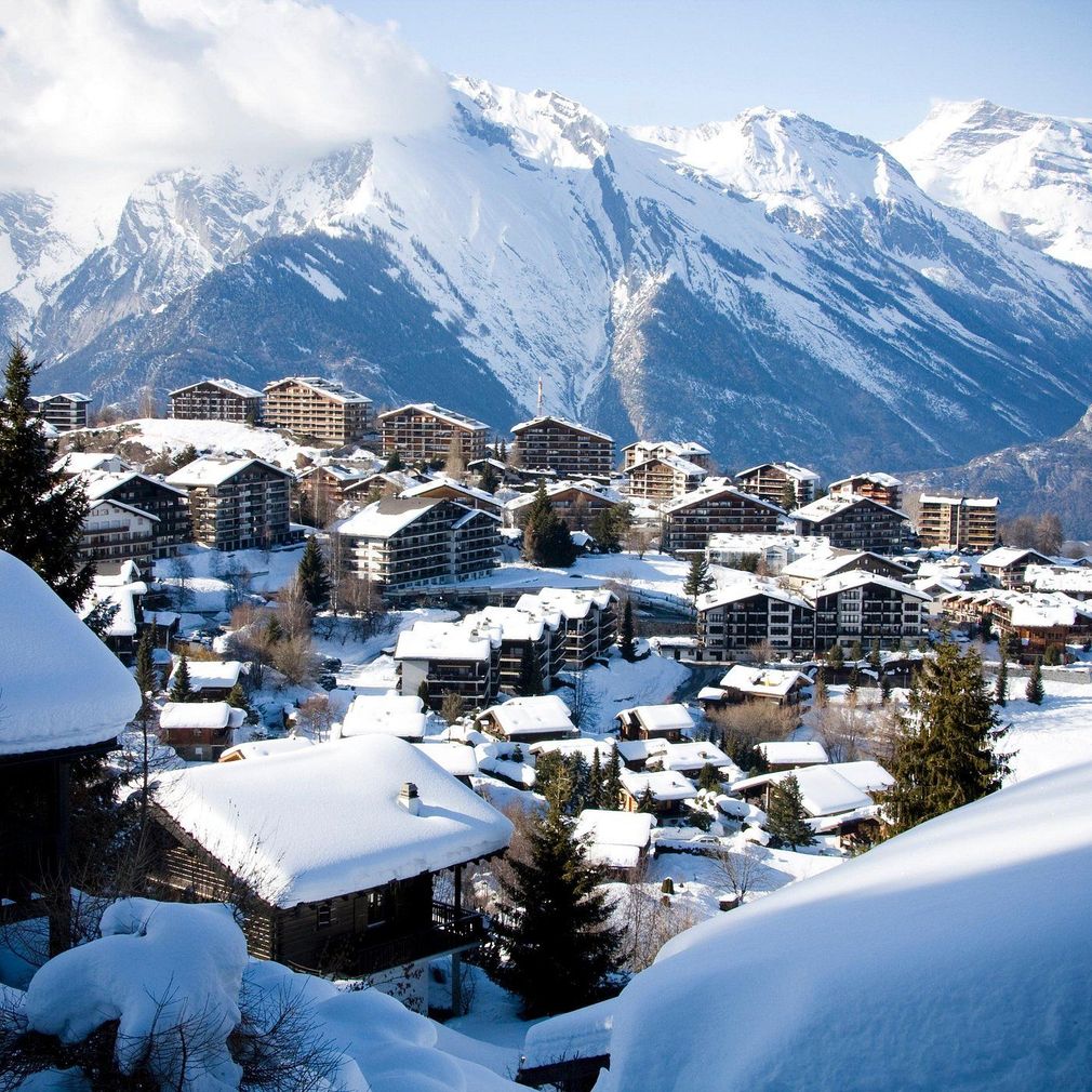 Village alpin enneigé, niché au pied de montagnes aux sommets enneigés, par une journée ensoleillée.