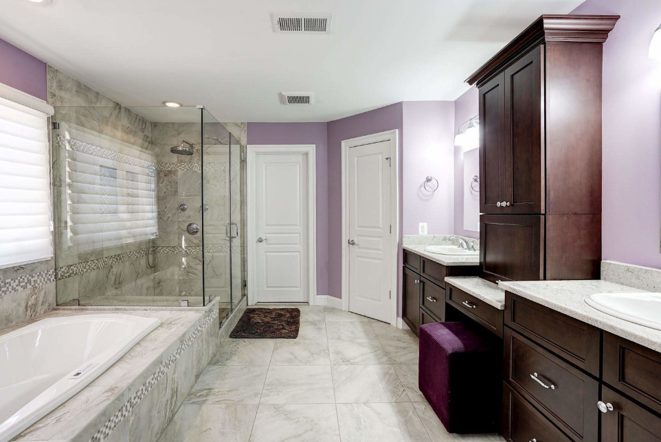 A bathroom with purple walls , a tub , two sinks , and a walk in shower.
