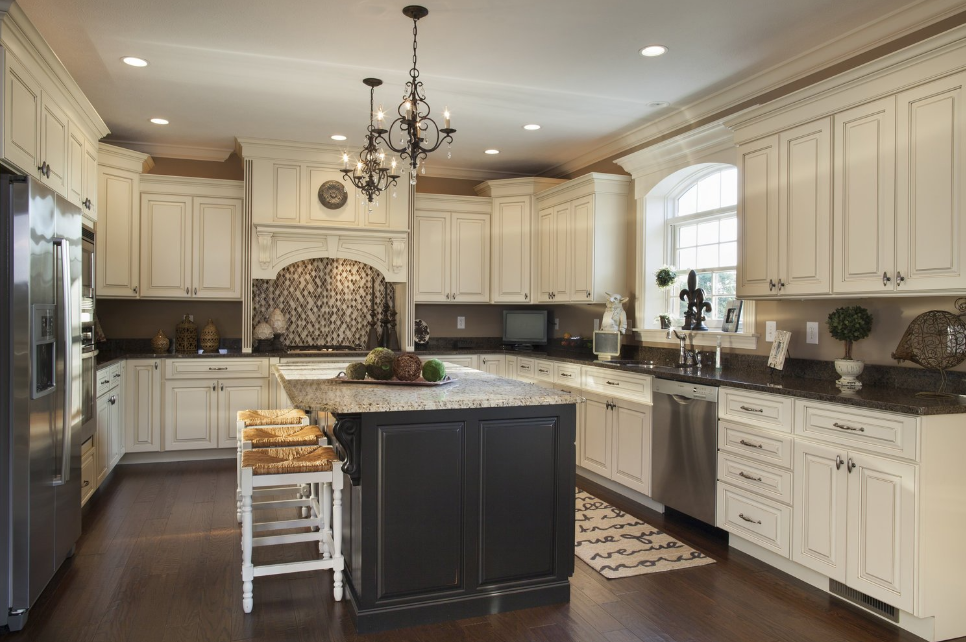 A kitchen with white cabinets , black counter tops , stainless steel appliances and a large island.