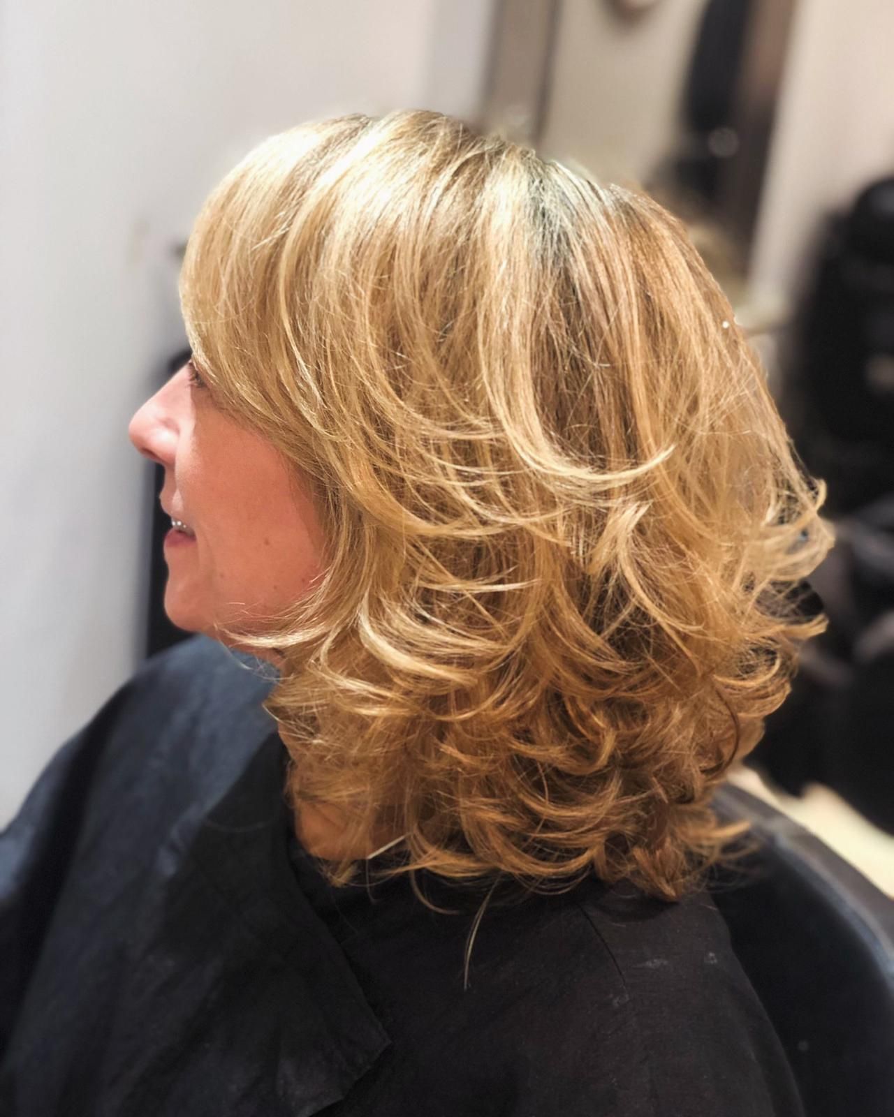 Side view of a layered blonde haircut with soft waves in a salon chair