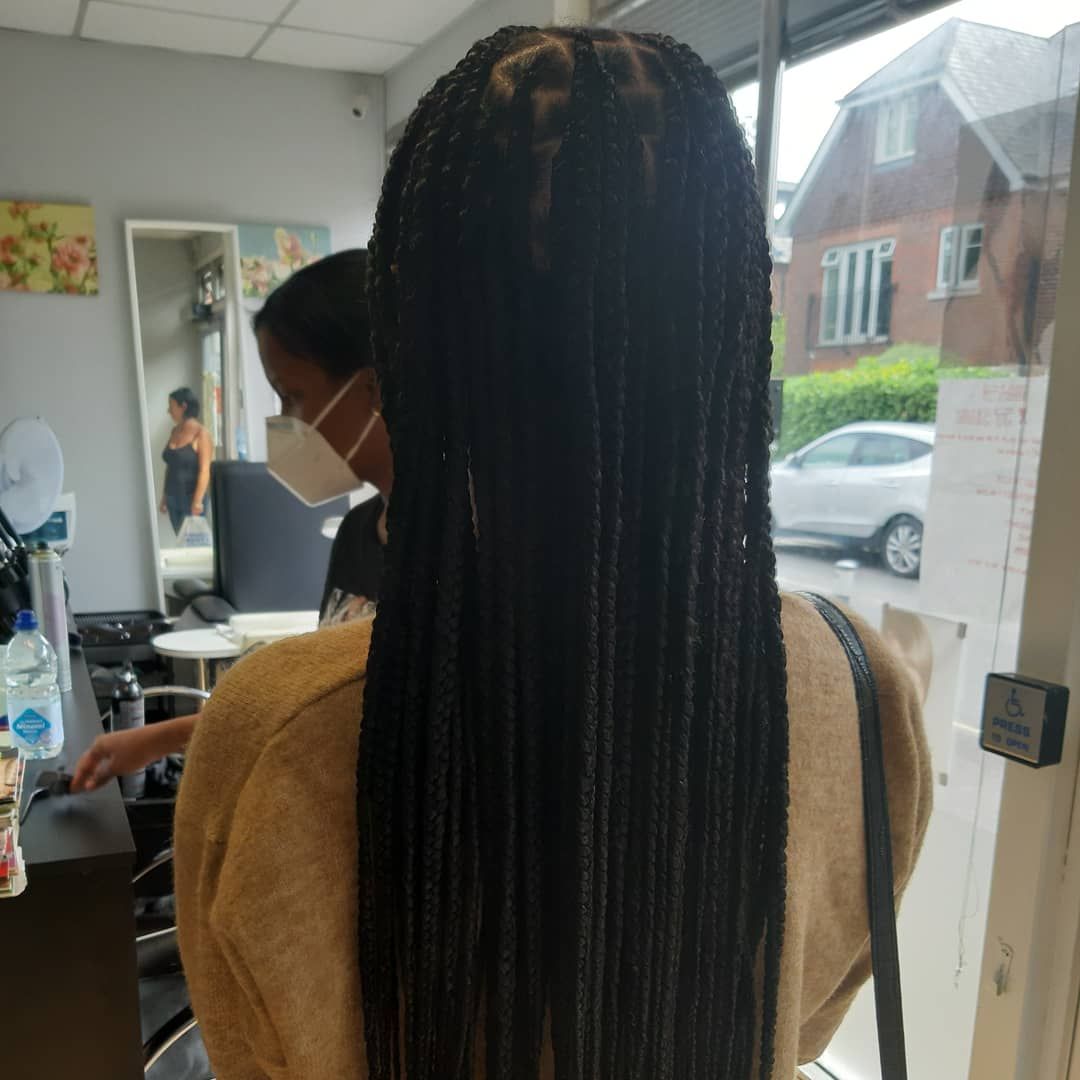 A woman wearing a mask and braids is standing in a salon.