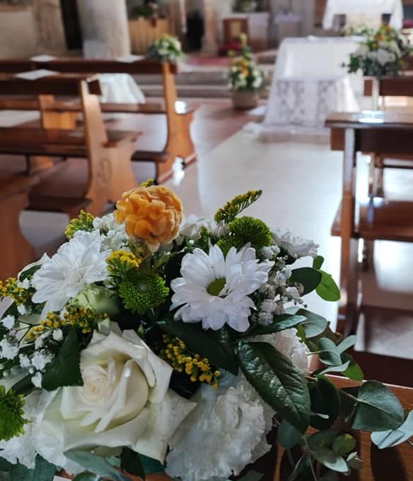 Un mazzo di fiori bianchi e gialli su un tavolo nella navata di una chiesa con banchi di legno.