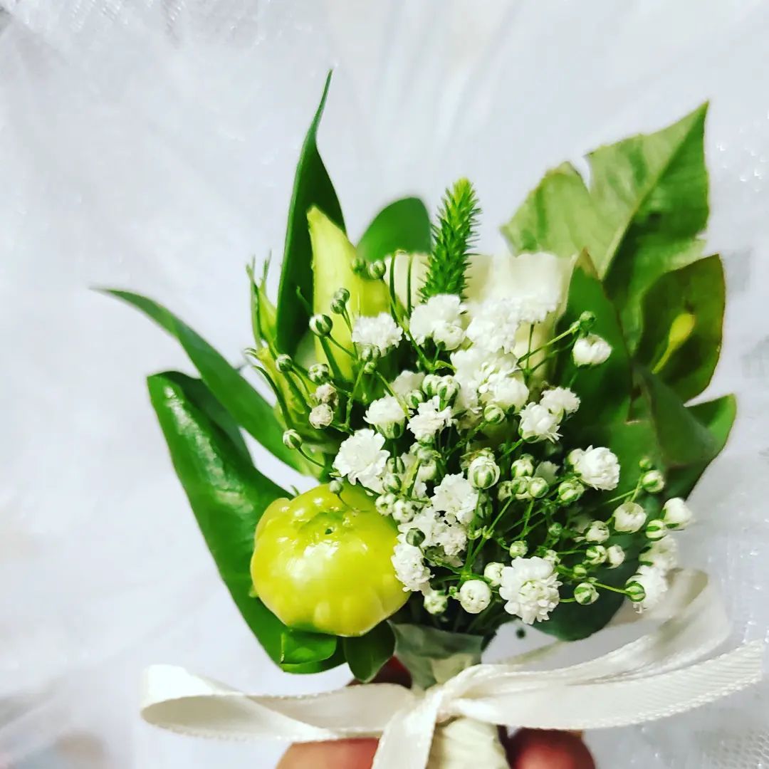 Bouquet di fiori bianchi con foglie verdi e un fiore giallo pallido legato con un nastro bianco.