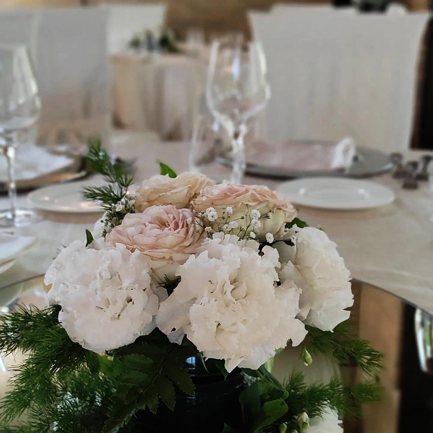 Centrotavola floreale con fiori bianchi e rosa pallido su un tavolo da banchetto con bicchieri da vino e piatti
