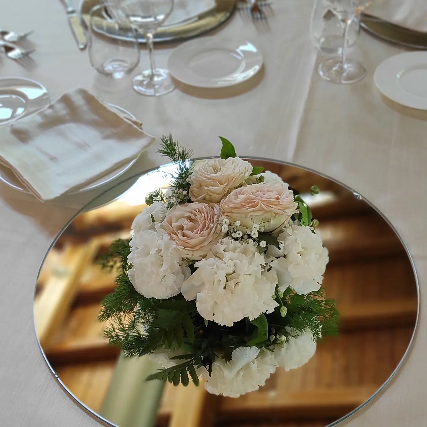 Centrotavola rotondo con specchio e fiori bianchi e rosa pallido su un tavolo da pranzo apparecchiato.