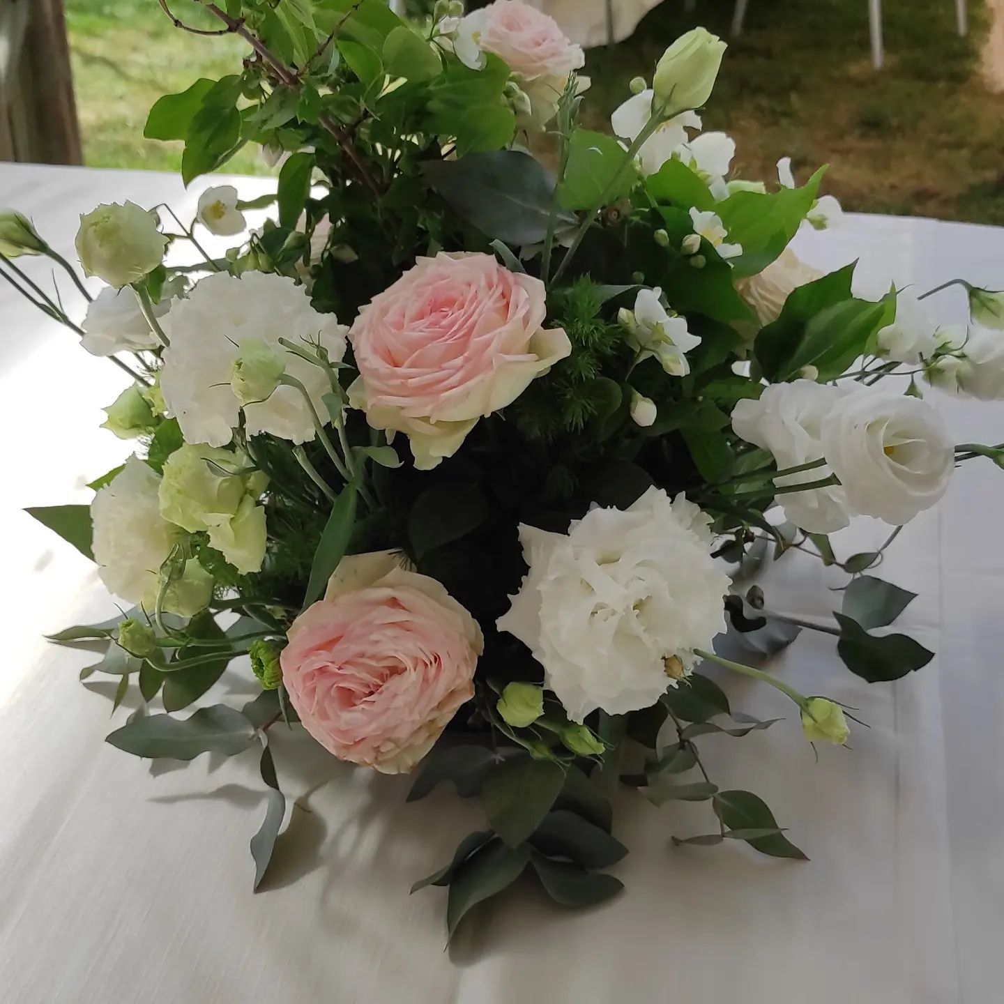 Bouquet di rose rosa e bianche con verde su una tovaglia bianca.