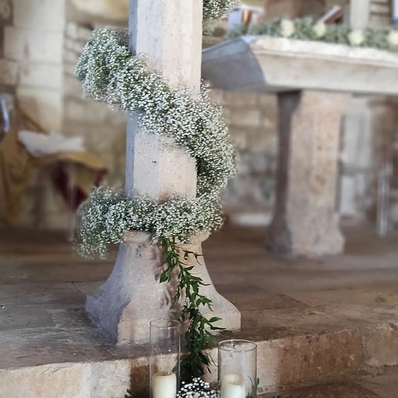 Fiori bianchi avvolti attorno a un pilastro di pietra accanto a piccole candele in un ambiente interno rustico