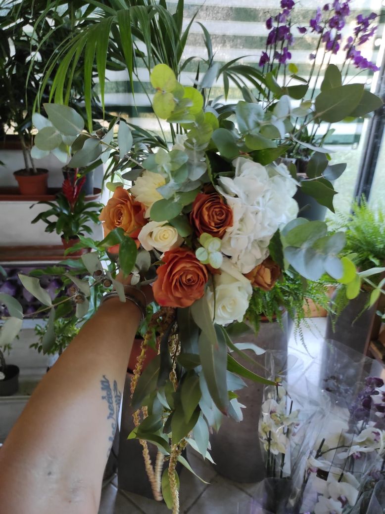 Un mazzolino di fiori arancioni, bianchi e viola con verde, tenuto in mano, in una stanza luminosa.