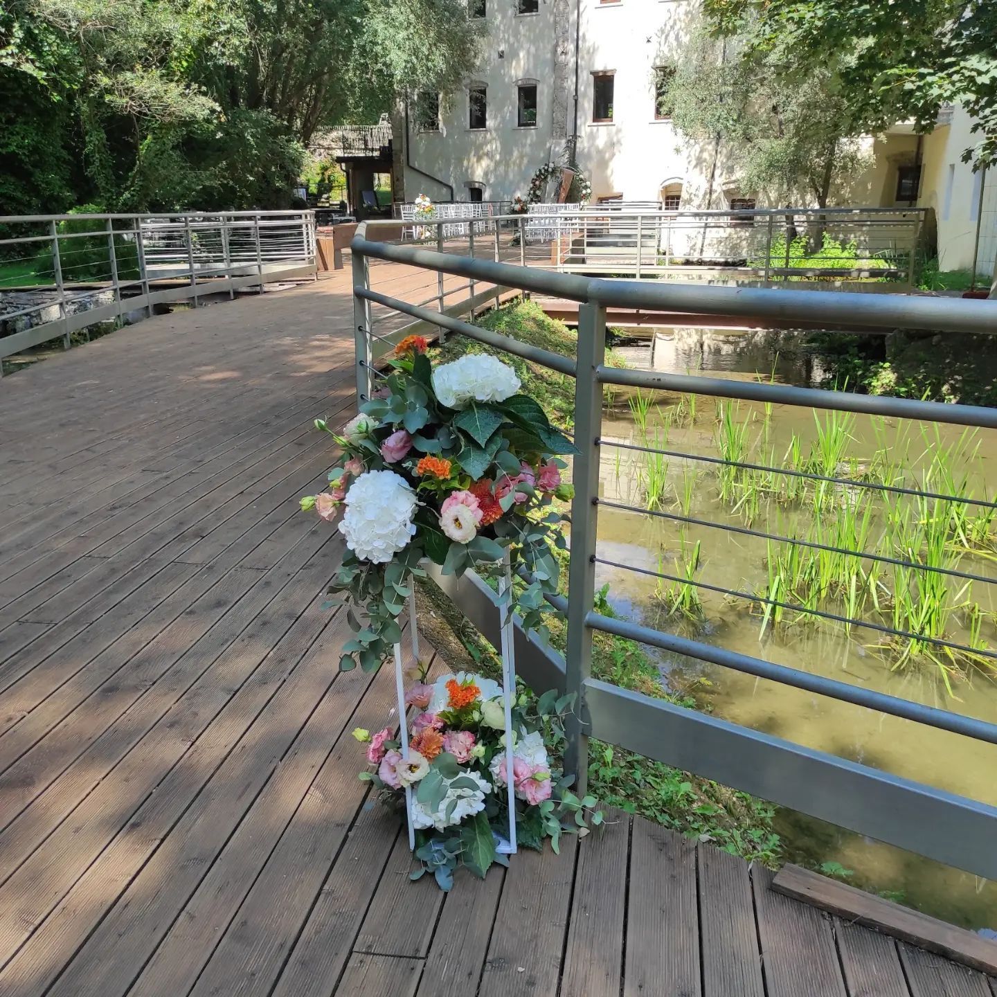 Composizioni floreali legate alla ringhiera di un ponte accanto a una passerella di mattoni e acqua verde