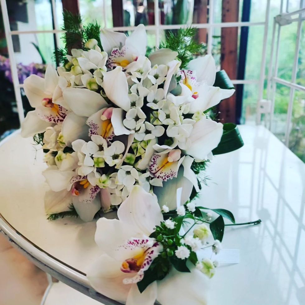 Bouquet da sposa bianco con orchidee e piccoli fiori su un tavolo riflettente, con una boutonnière abbinata nelle vicinanze.