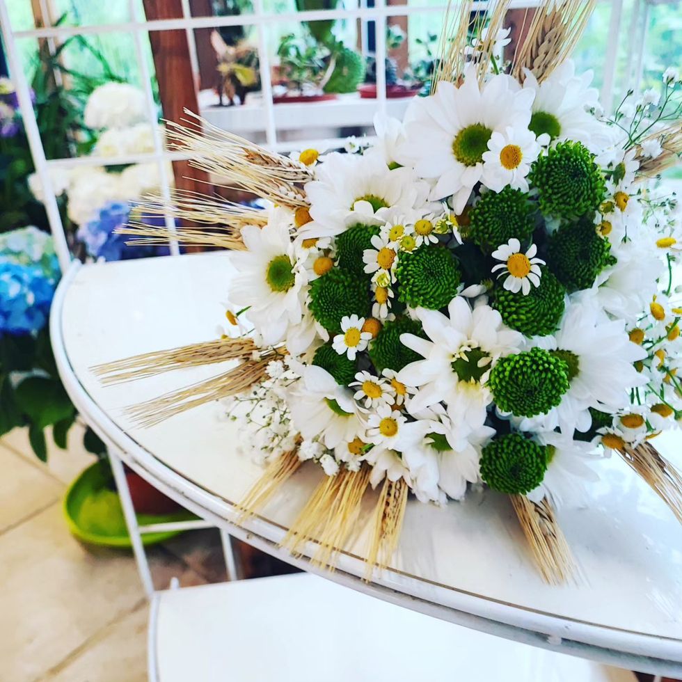 Bouquet floreale bianco e verde con margherite e dettagli dorati su un tavolo bianco.