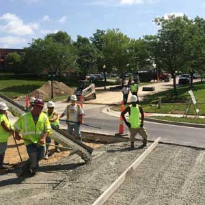 Construction workers pouring concrete on a road with trees and cars in the background. Sunny day.