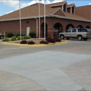 Brown brick building with arched windows, a paved driveway, and parked SUVs under a blue sky.