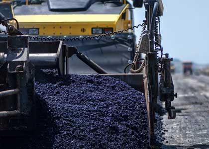 Asphalt being laid on a road by a yellow paving machine; black asphalt in foreground.