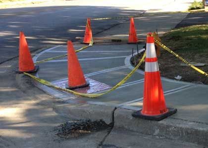 Freshly poured sidewalk, orange cones, yellow caution tape; road work site.