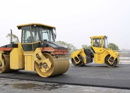 Two yellow road rollers compacting asphalt on a road, outdoors.