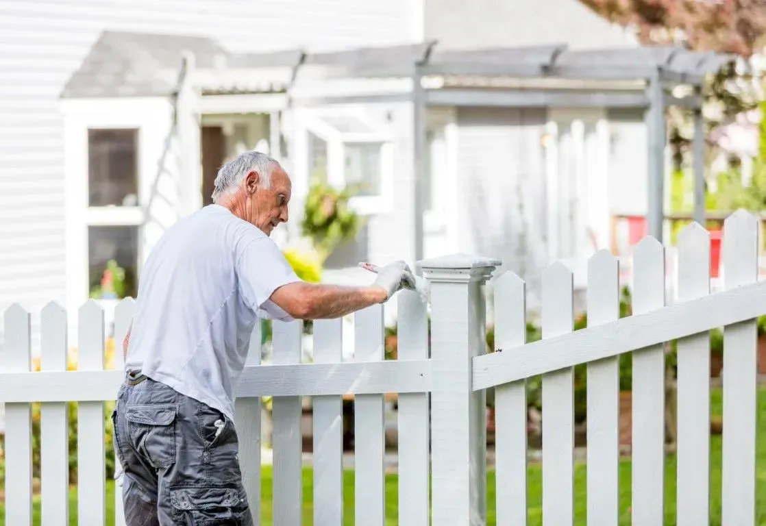 Man repairing white picket wooden fence