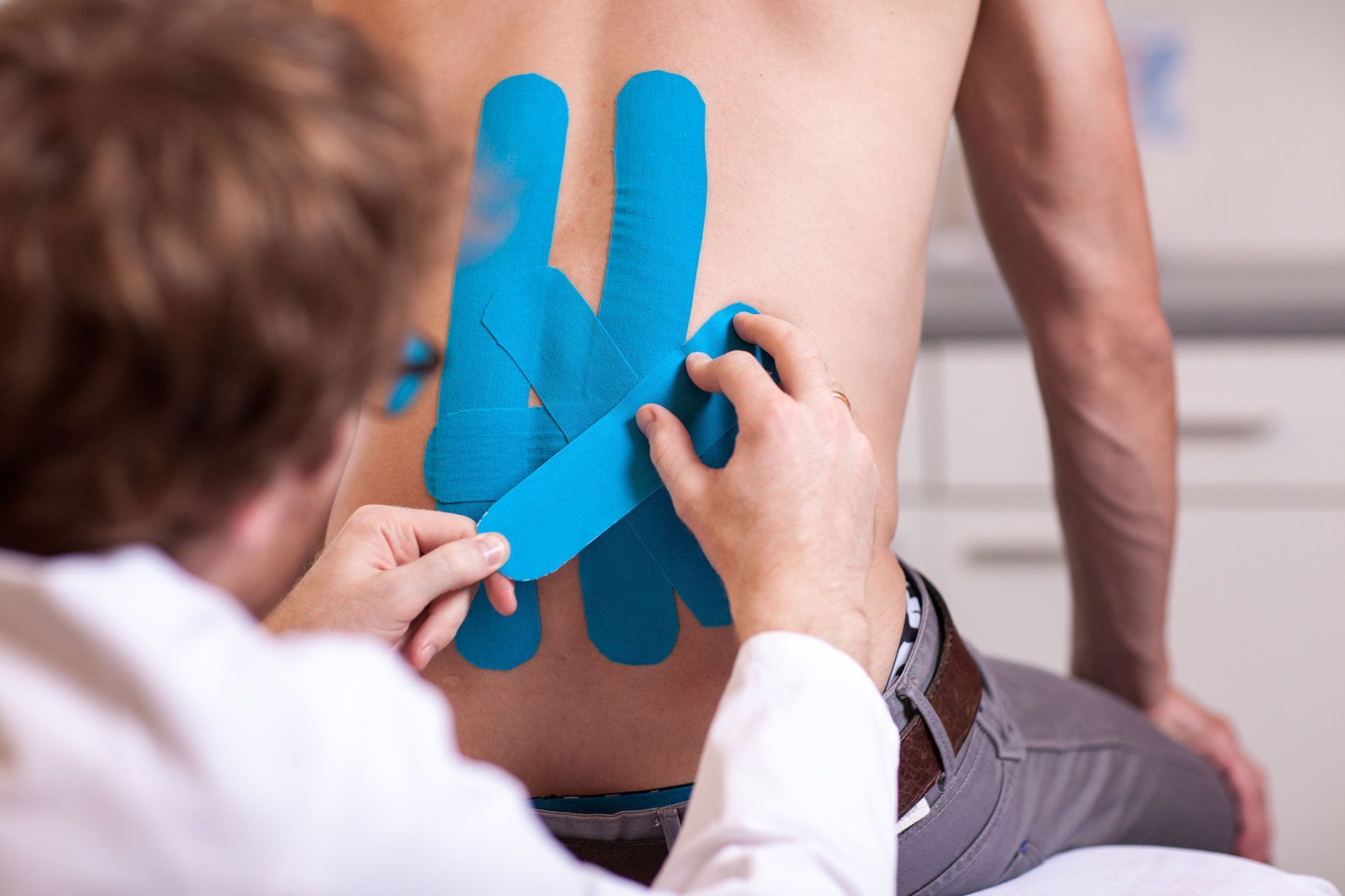 Taping, Arzt klebt blaue Taping-Bänder auf den Rücken