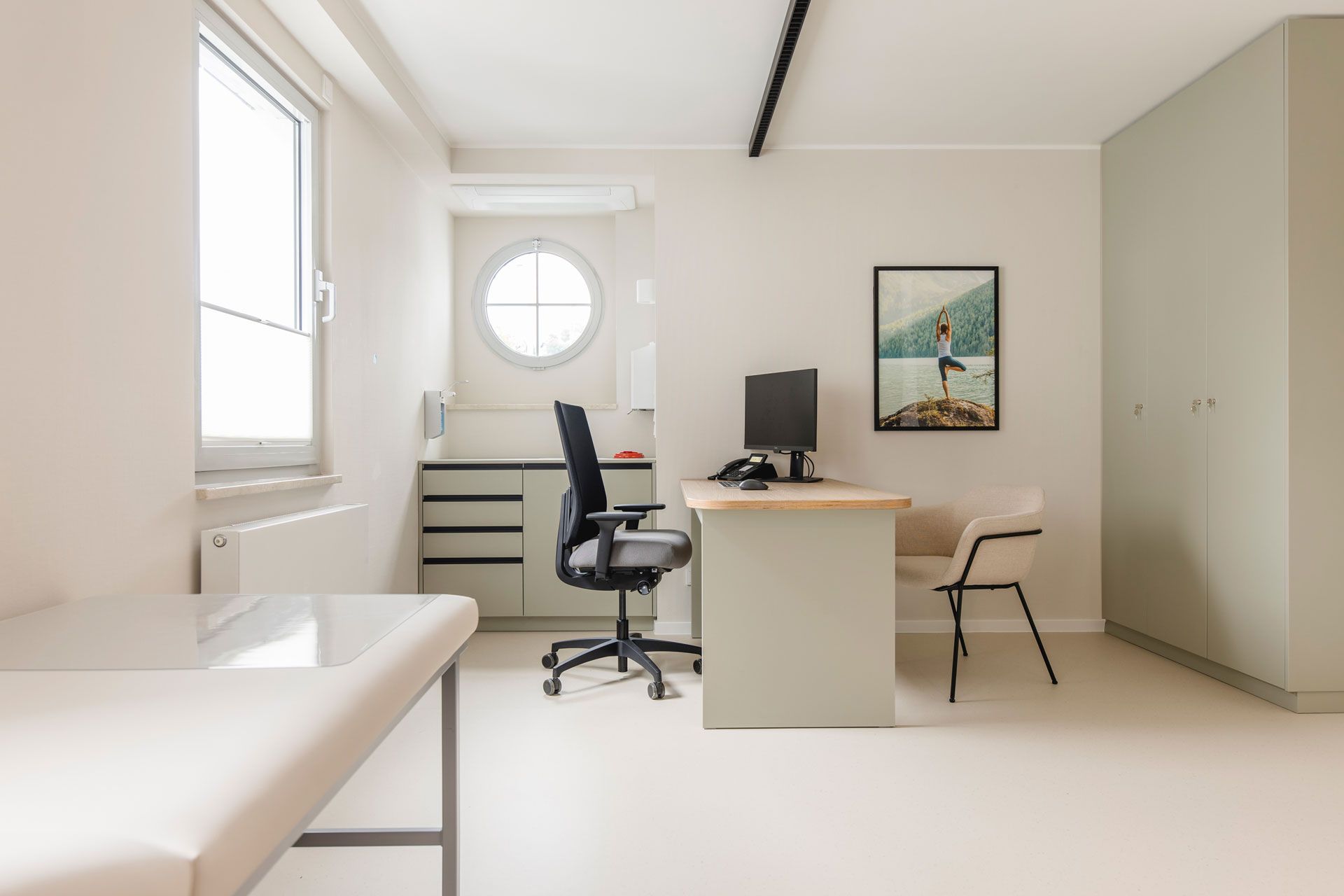 Freundliches Sprechzimmer mit einem Holzschreibtisch, Liege, Bullauge, an der Wand ein Bild mit einer Fra