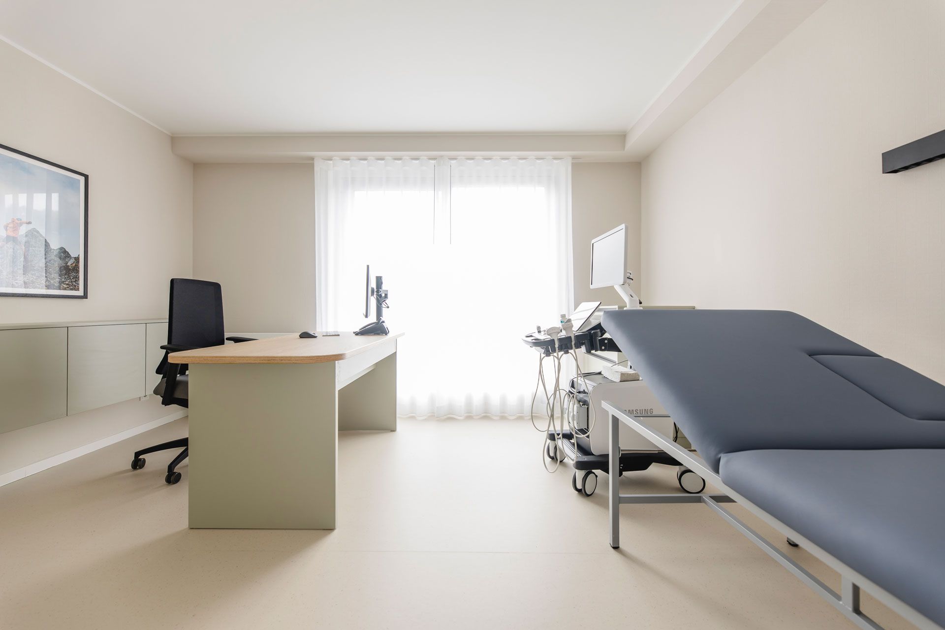 Sprechzimmer mit mintfarbenen Möbeln und einer dunkelblauen Liege, Ultraschallgerät, sehr auferäumt, freundliches Behandlungszimmer